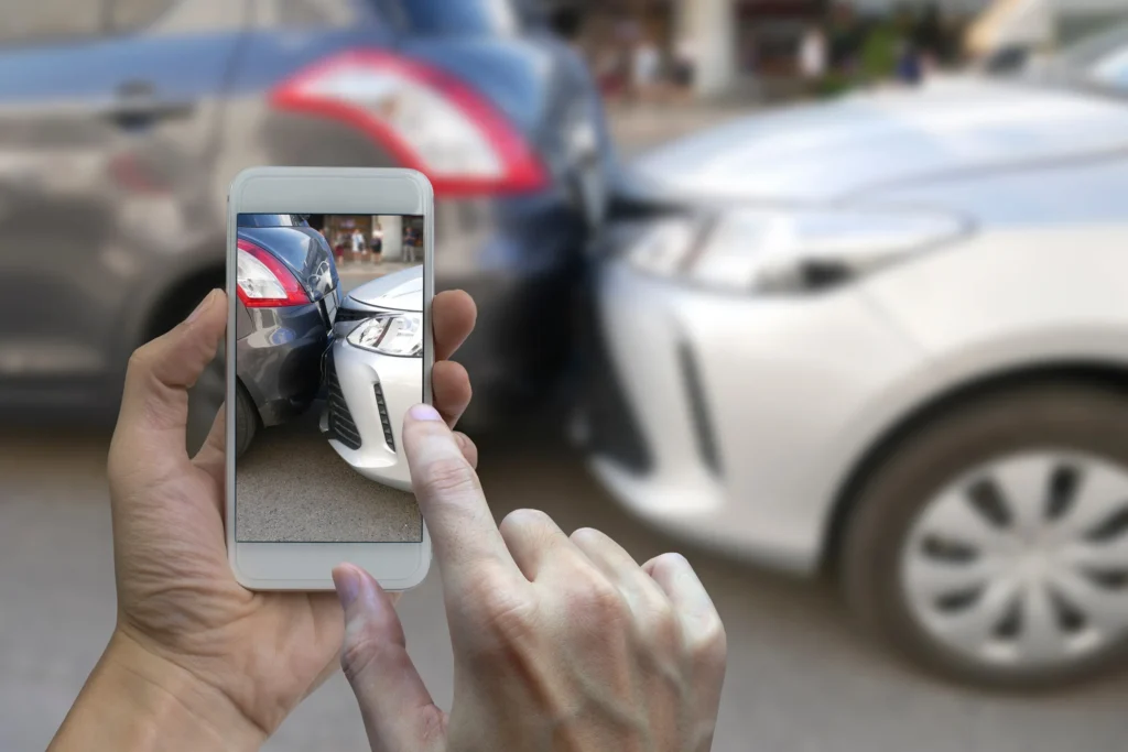 A person taking a photo of a car accident scene between two cars.