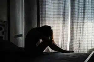 A woman sits on a bed with her head down, conveying sadness or emotional distress