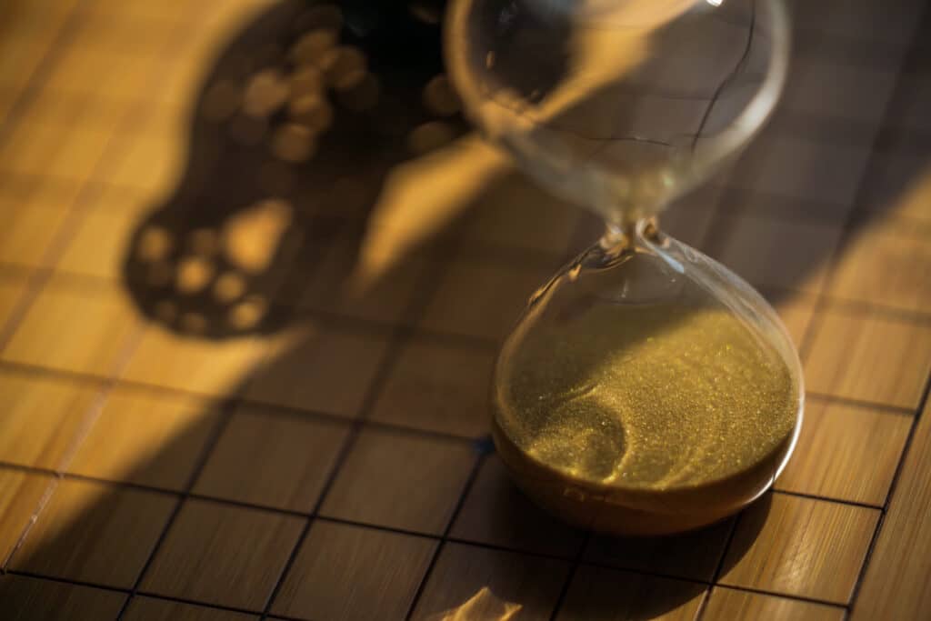 An hourglass with gold sand on a grid-patterned board in warm afternoon light