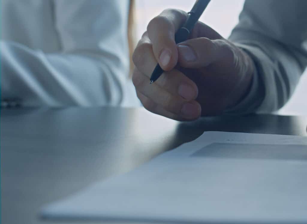 A close view of one hand holding a pen above a printed agreement on a desk