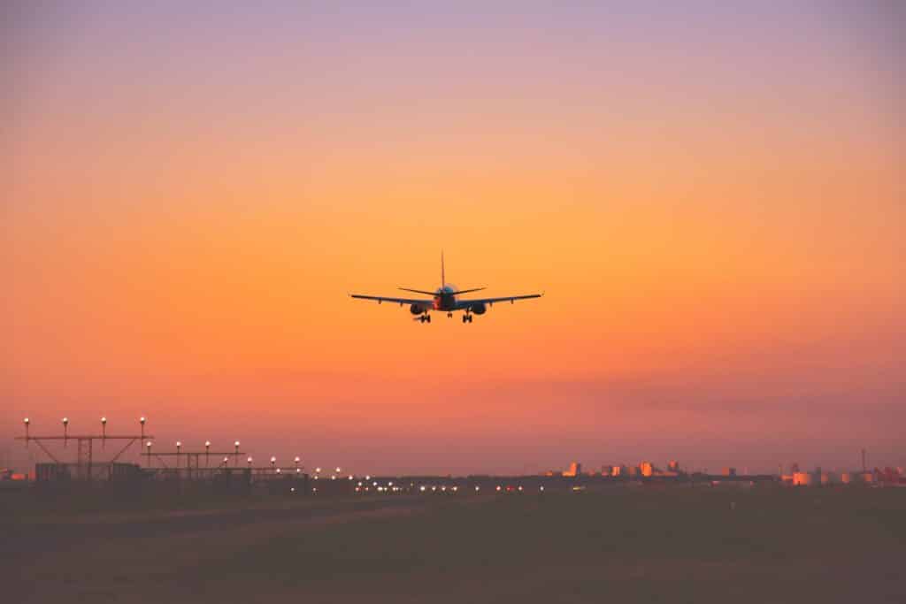 A passenger aircraft silhouetted against an orange sky on final approach at dusk