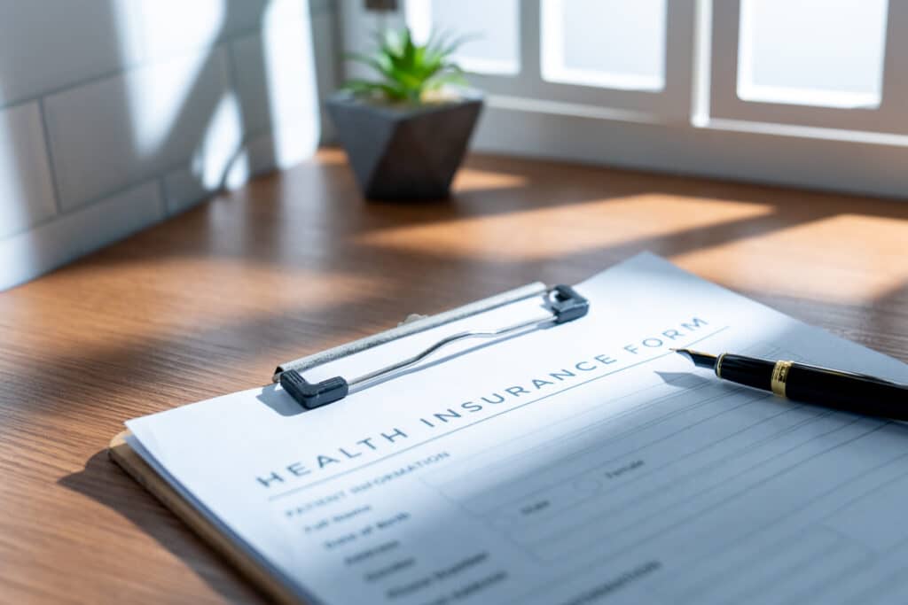An insurance form on a clipboard with a pen, on a wooden desk in natural light