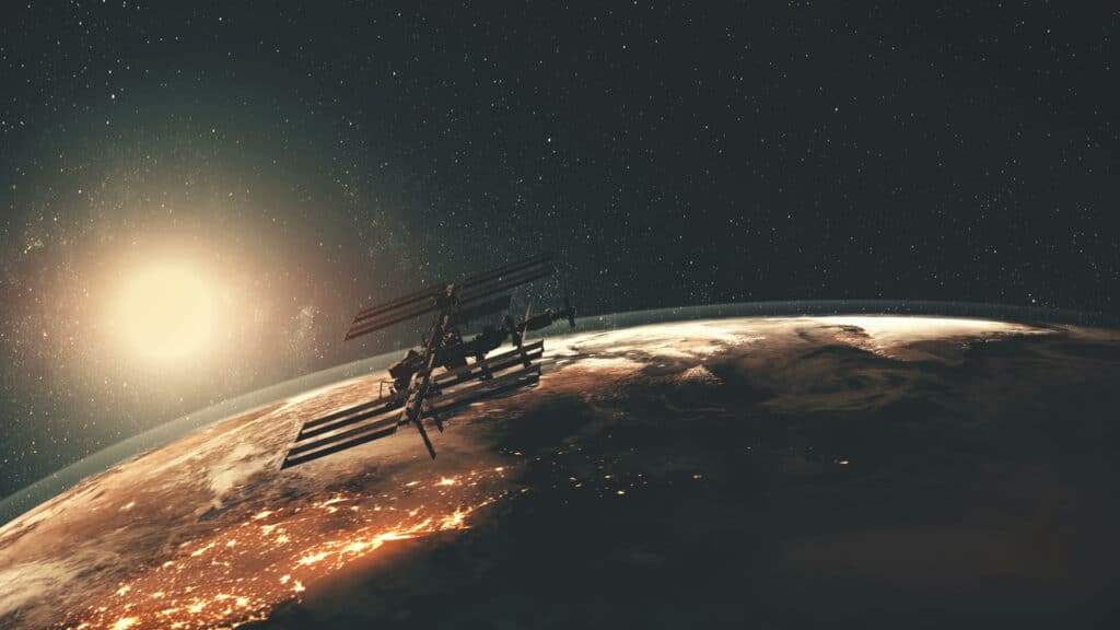 A satellite in orbit above Earth against a starfield, with sunlight along the horizon