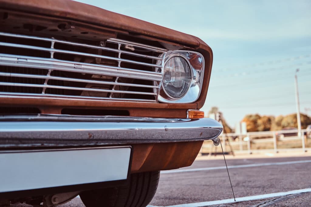Close detail of a vintage car's chrome bumper and grille on a sunlit street
