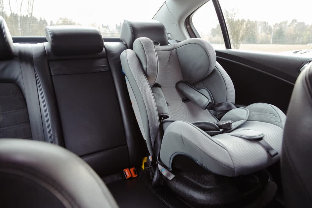 An empty gray child car seat installed on the back seat of a car in soft daylight